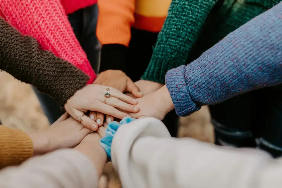 A circle of people placing their hands together to show shared support and community solidarity.